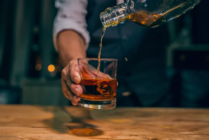 A bartender pouring whisky from a glass bottle into a glass