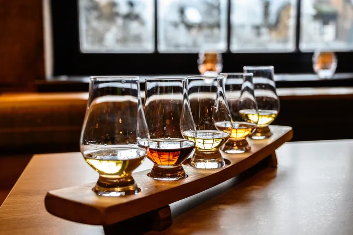 5 glasses of various whiskey to select standing next to each other on a wooden board with more glasses on background