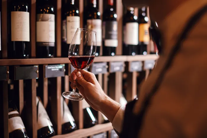 a sommelier swirling wine in a glass with wine bottles in the background 
