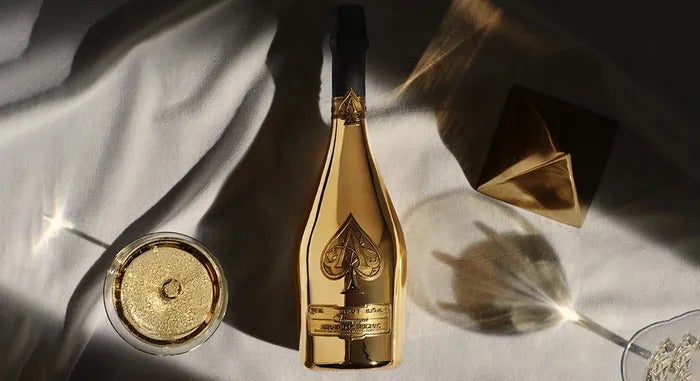 Bottle of Armand de Brignac Champagne next to wine glass resting on elegant white sheets