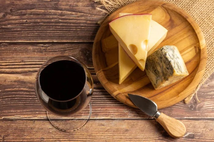 a glass of red wine next to a cheese board and a knife with different types of cheese