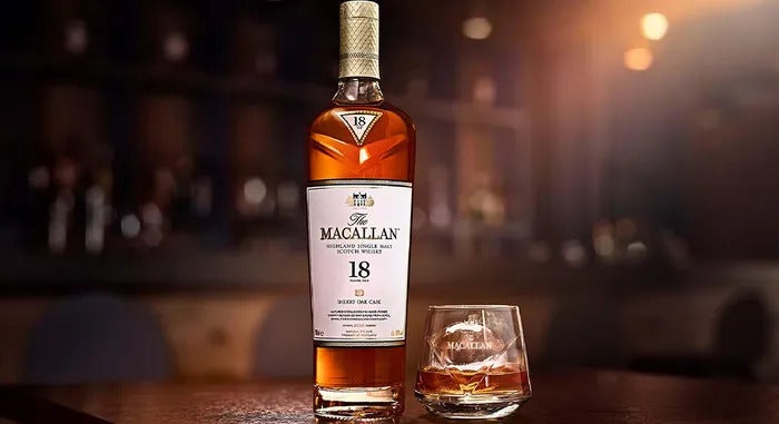 Bottle of the Macallan 18 year sherry oak whisky next to a tumbler of whisky on a bar counter