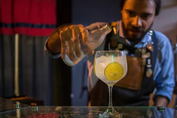 A bartender pouring gin from a glass bottle to a glass with glass and a lemon