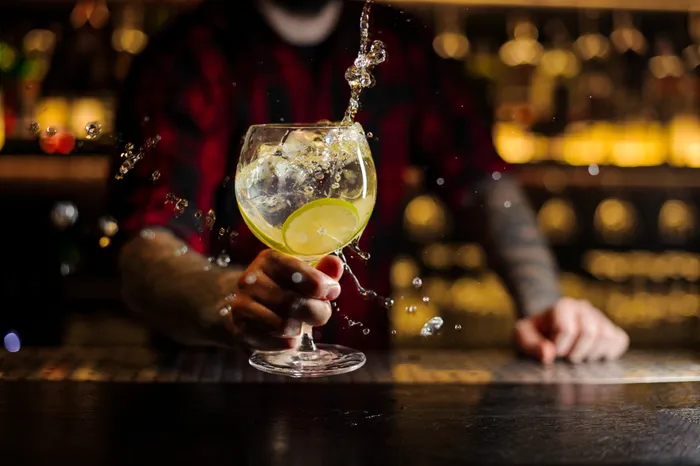a bartender passing you a glass of gin with a slice of a lime