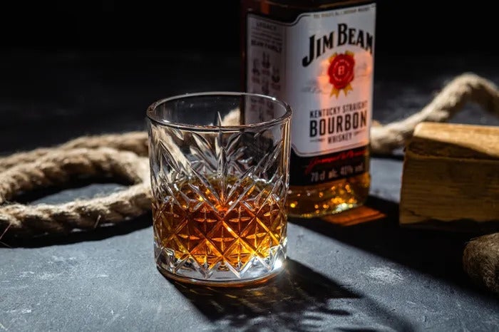A glass of neat Jim Bean Bourbon next to a fresh bottle and thick rope