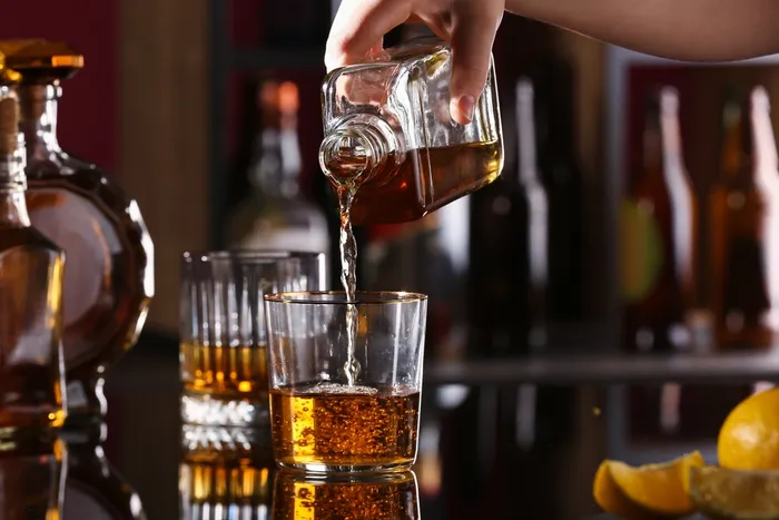 pouring single malt whiskey from a glass bottle into a short glass with more whiskey in the background and some oranges in the foreground