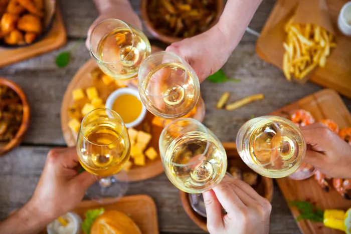People clanking glasses of white wine with a plenty of suitable food on the table